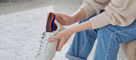 Person inserting an insole into a white sneaker.