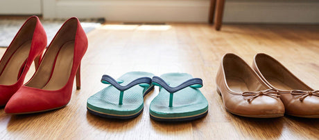 High heels, flip-flops, and ballet flats arranged side by side on a wooden floor.