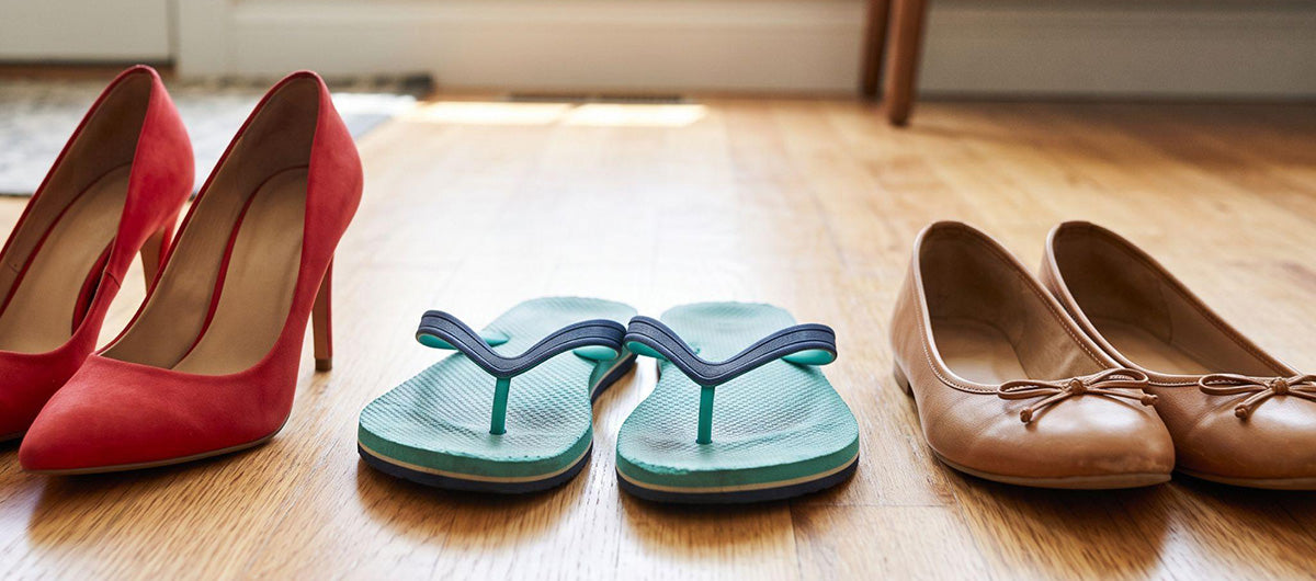 High heels, flip-flops, and ballet flats arranged side by side on a wooden floor.