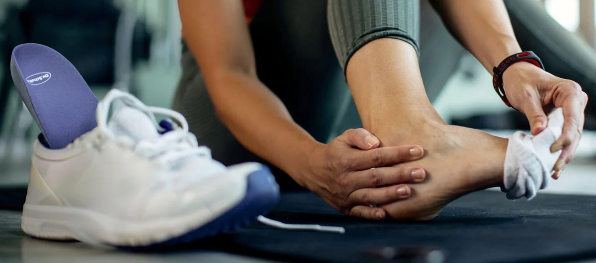 Woman holding heel and side of foot with tennis shoe on the side.