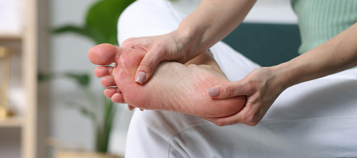 A person holding the bottom of a bare foot and heel suffering from plantar fasciitis pain.