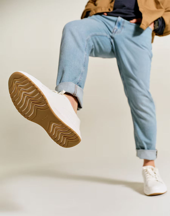 Person wearing light blue jeans and white sneakers with a beige sole on a plain background