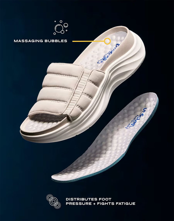White sandal with a sole displaying 'Massaging Bubbles' and 'Distributes Foot Pressure' text on a dark background.