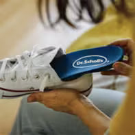 Person using a blue Scholl shoe stretcher on a white sneaker.