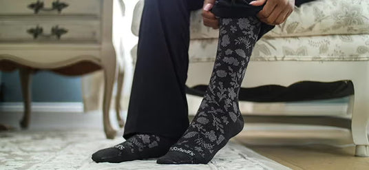 Person wearing black floral-patterned socks in a home setting.