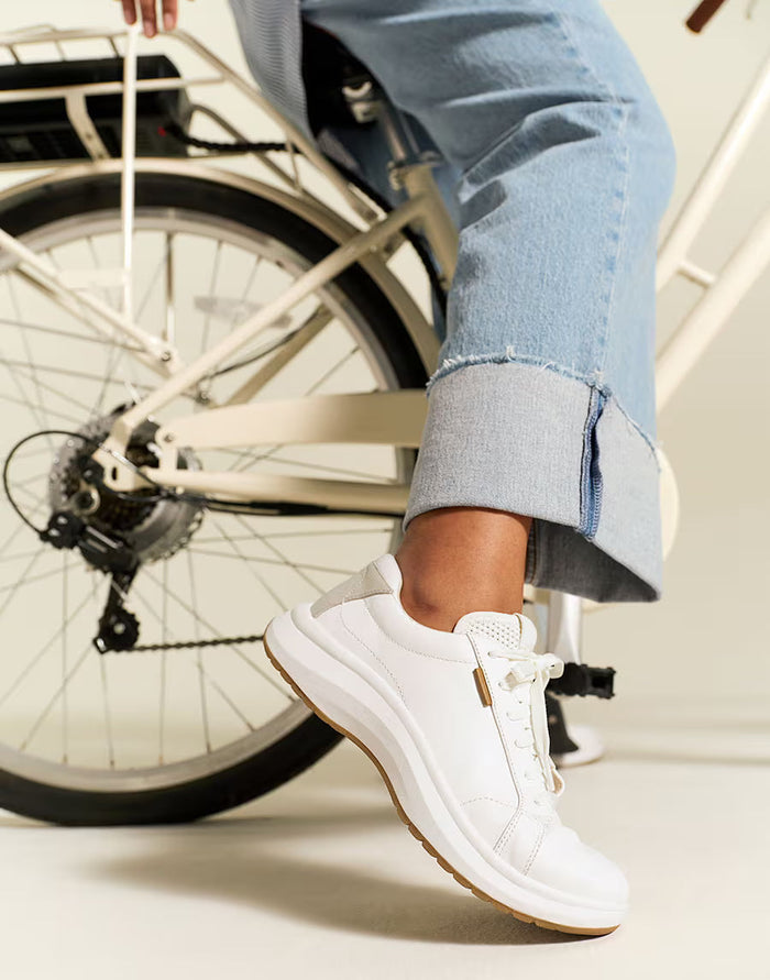 White sneakers with brown soles worn by a person sitting on a bicycle.