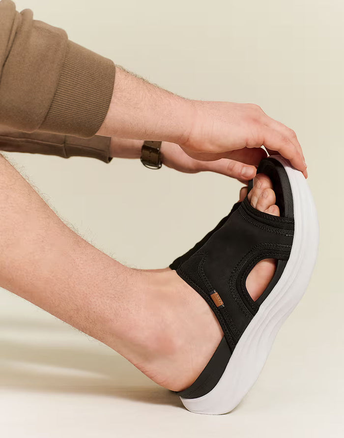 Person wearing a black sandal with a white sole on a beige background